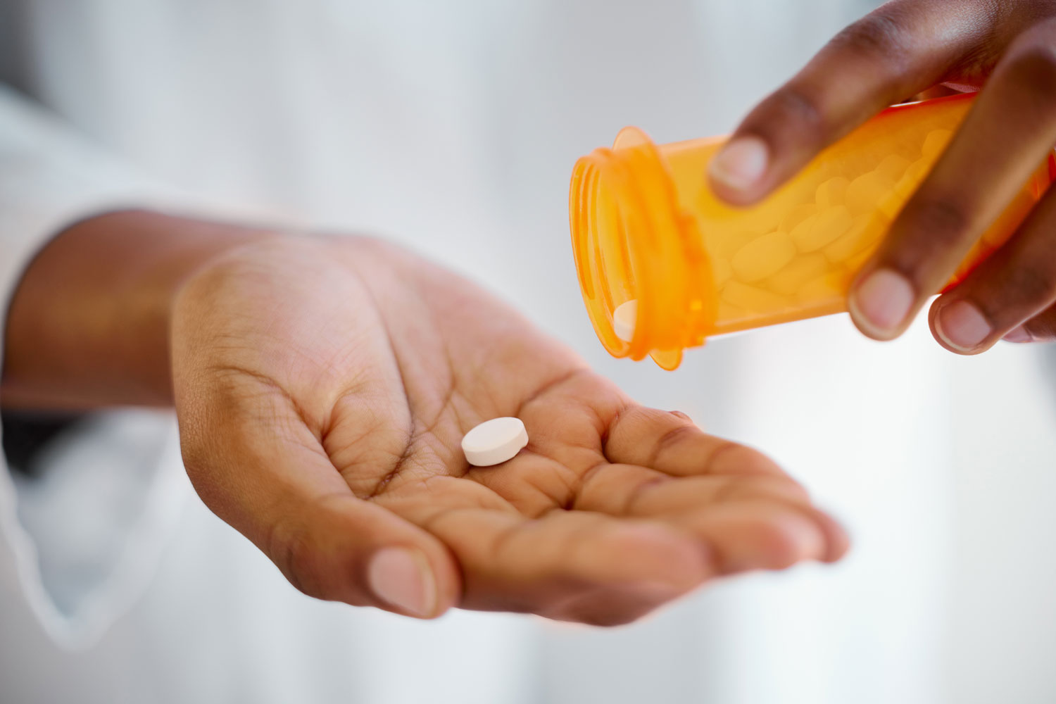 Person in a white coat holding a prescription medication bottle and pouring out white tablets